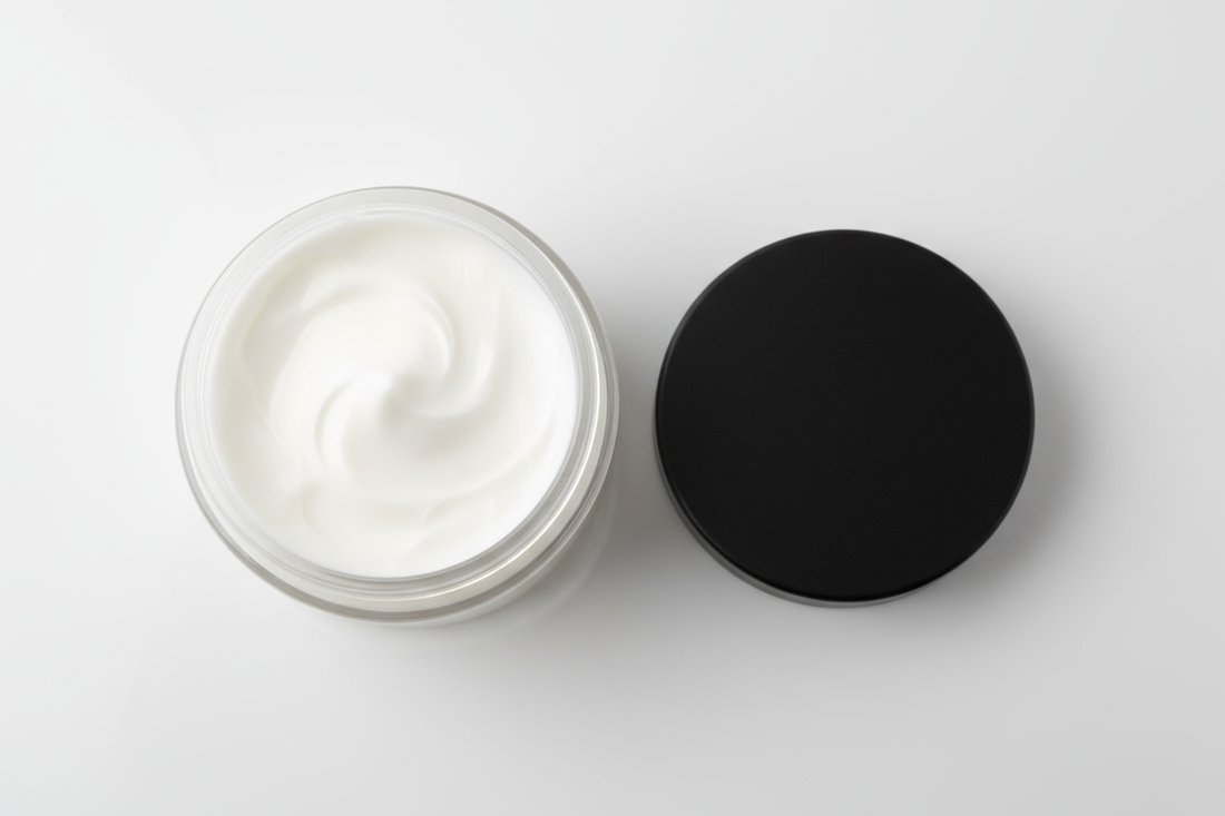 4oz clear plastic jar with black lid sitting next to it. Looking down into the jar a white cream